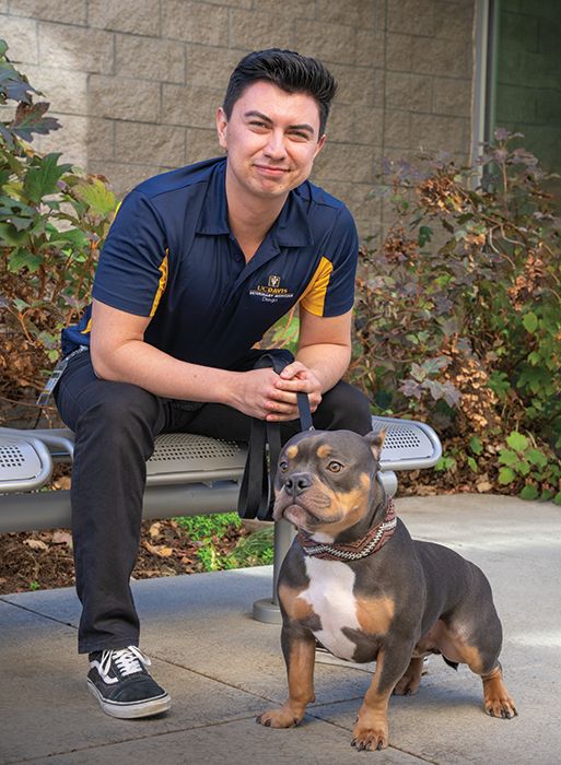 DVM student Diego Roque Aguayo sitting on a bench with Louis, the dog.