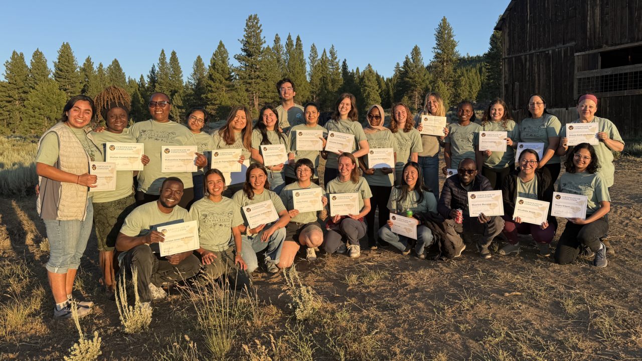 A group of people with certificates posing in front of a barn in the evening sunlight.