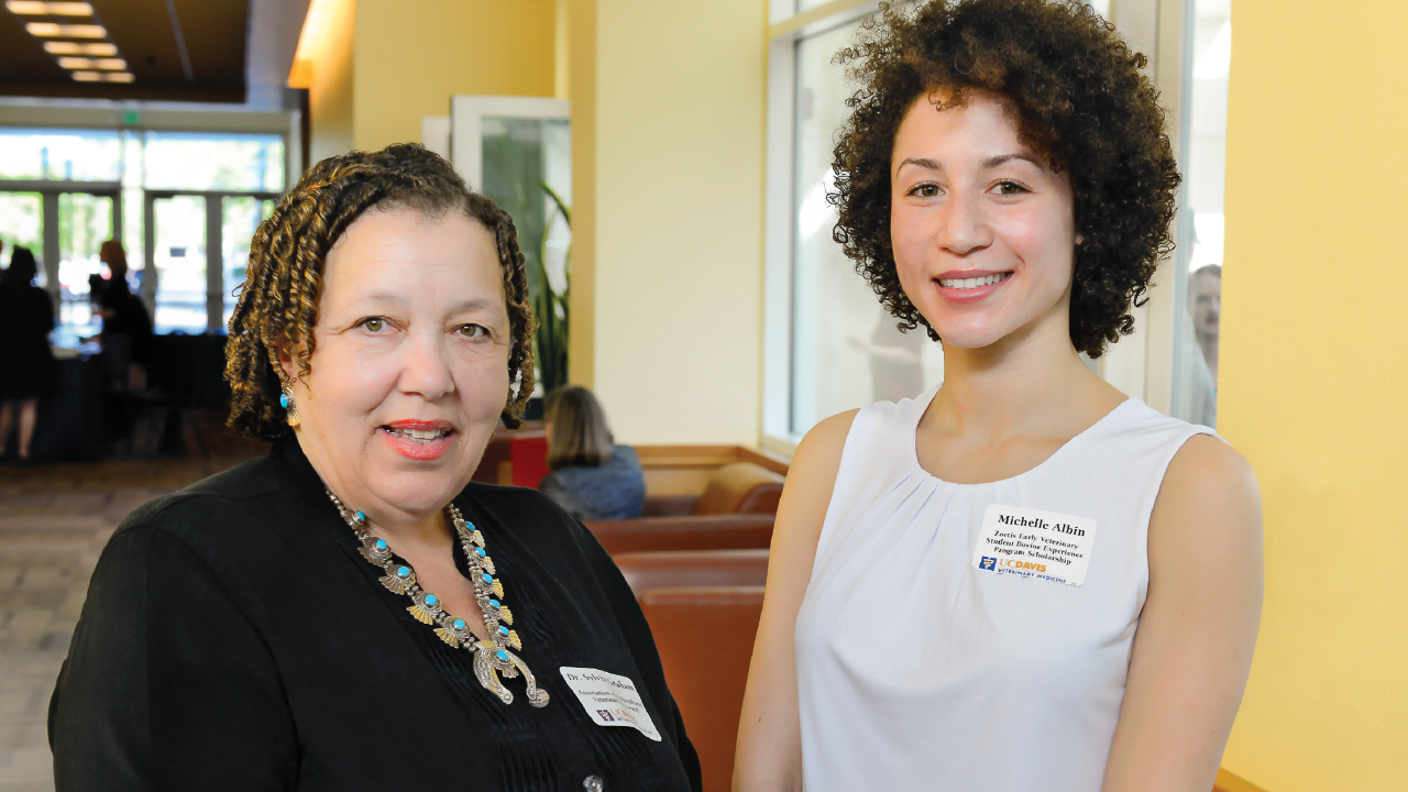 Two women smiling at an event inside.