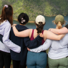 A group of five vet students with arms around each other stand at top of a hill overlooking a lake.